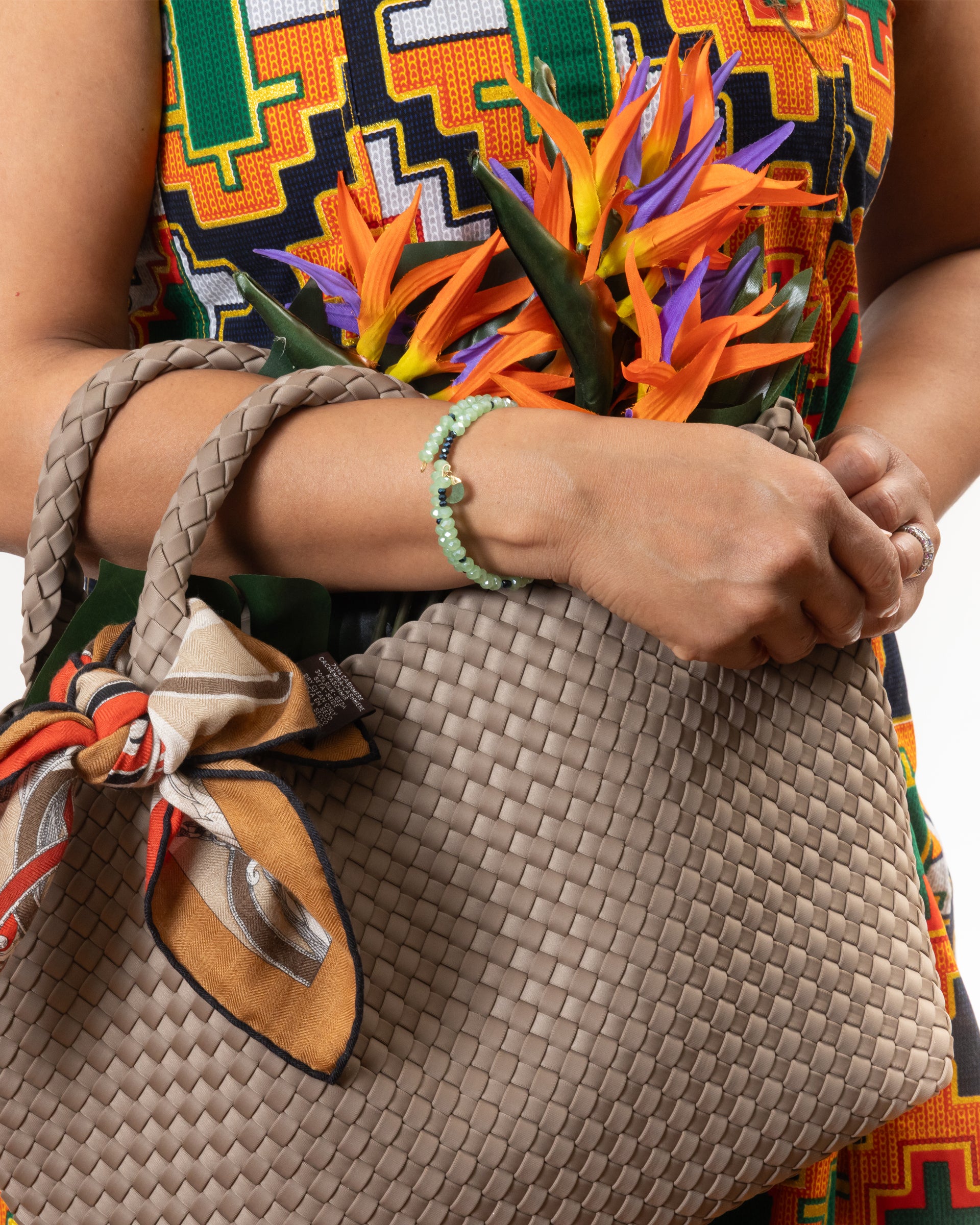Person holding a woven beige handbag wearing the choker bracelet with colorful fabric in the background